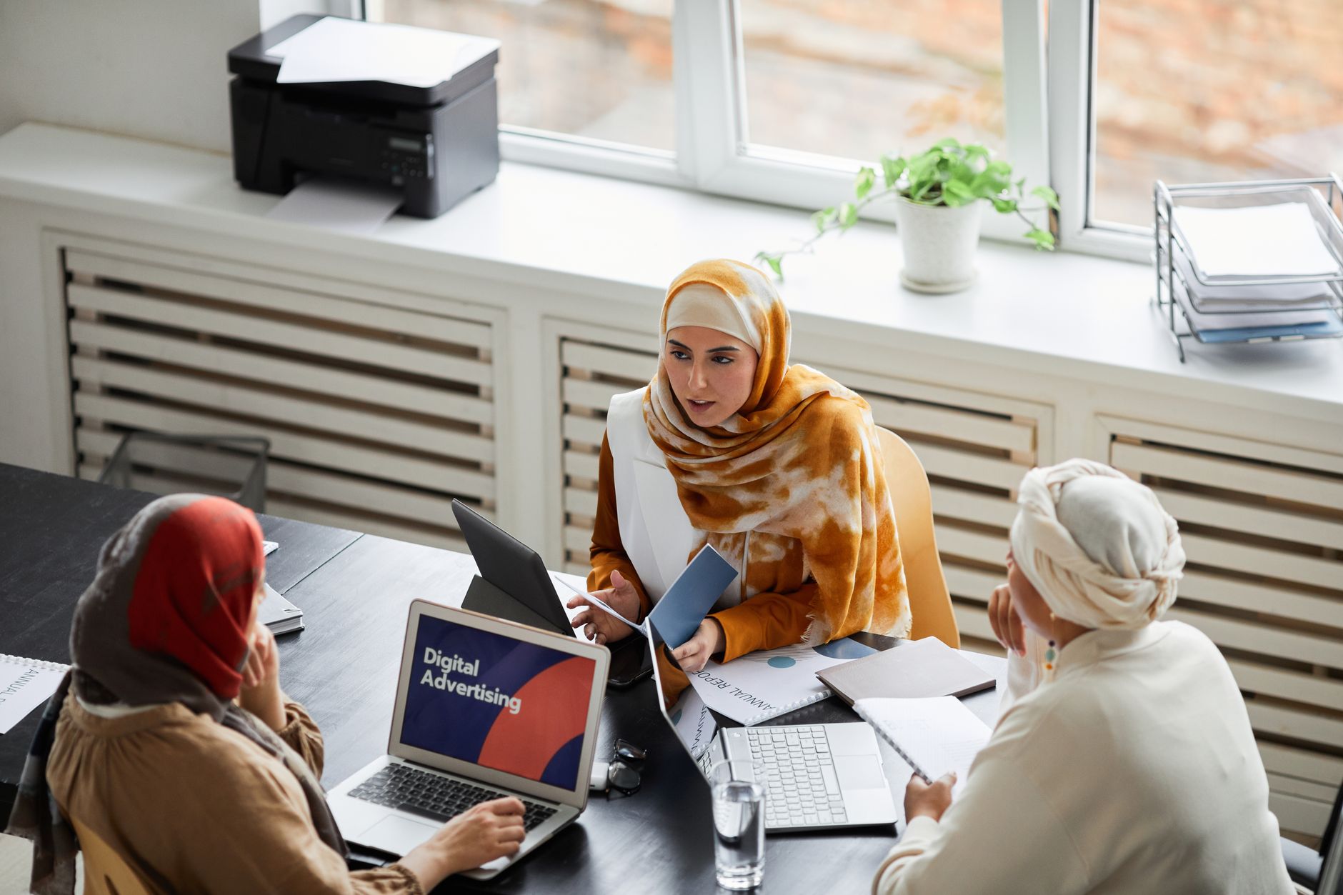 Three people discuss digital advertising at a table in a modern office