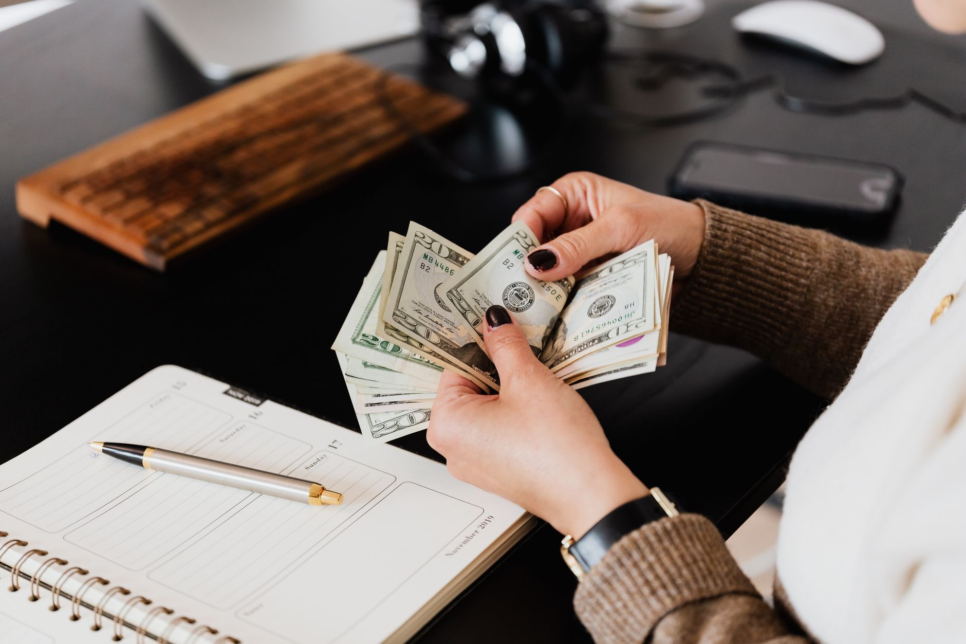 Hands count US dollars over an open planner, budgeting for event costs