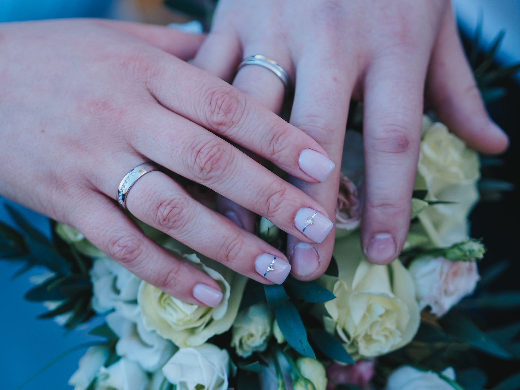 Two hands wearing wedding rings are clasped over a bouquet of roses