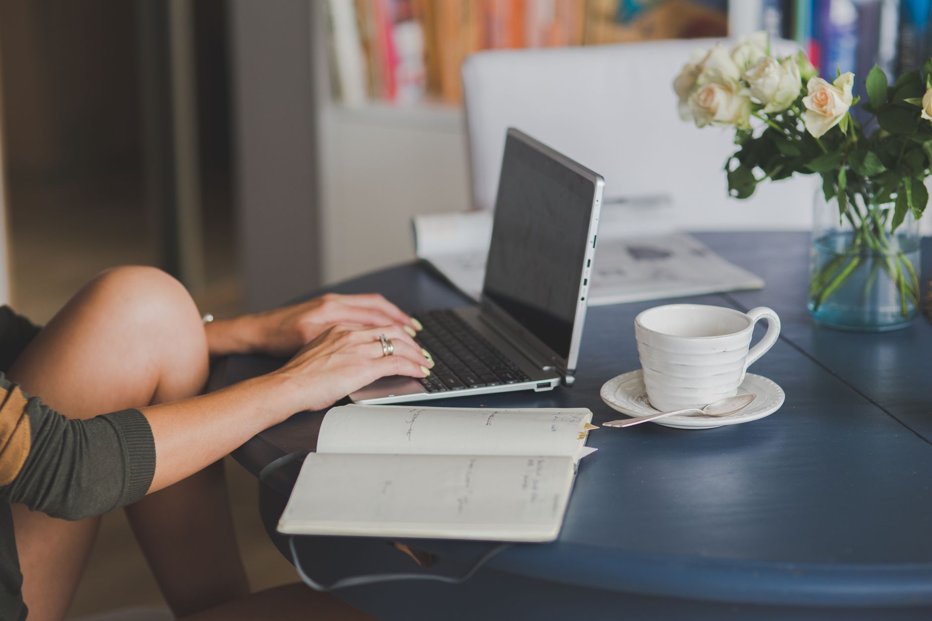 A person uses a laptop at a table with a notebook, coffee, and flowers