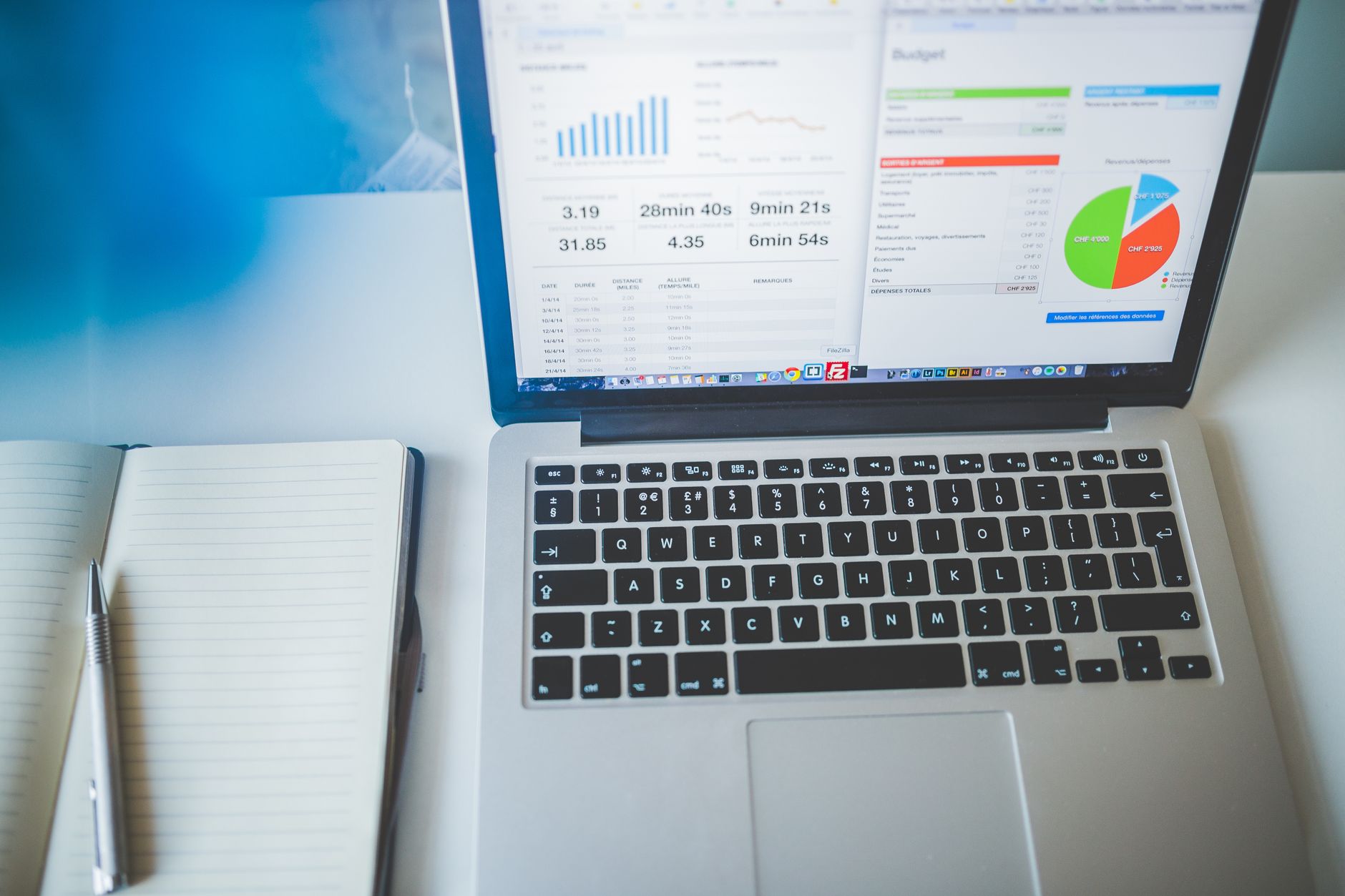 Laptop displays data charts and graphs, with a notebook and pen nearby