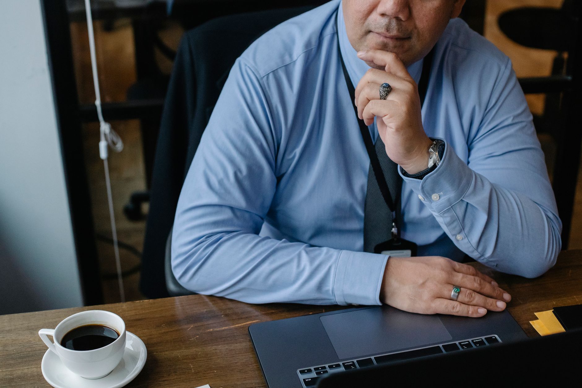 A man in a blue shirt touches his chin beside an open laptop