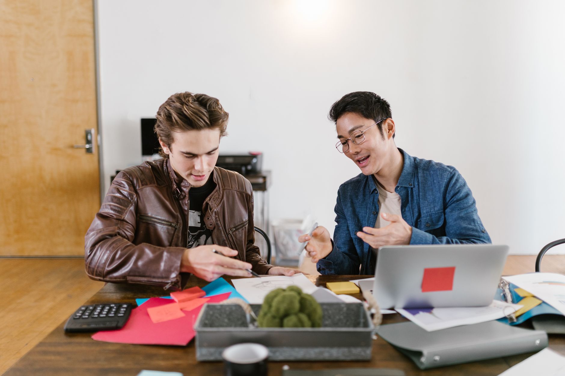 Two men collaborate on service branding concepts with papers and a laptop
