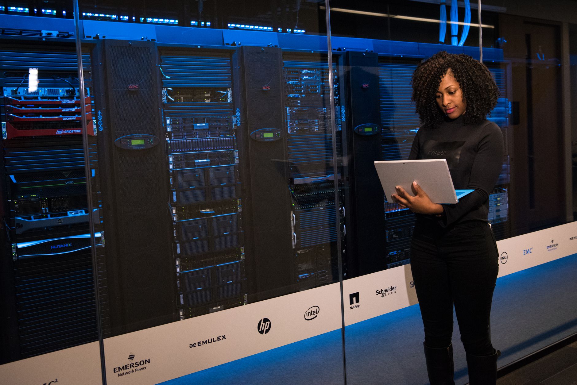 Woman holds a laptop in front of server racks with blue lights in a data center
