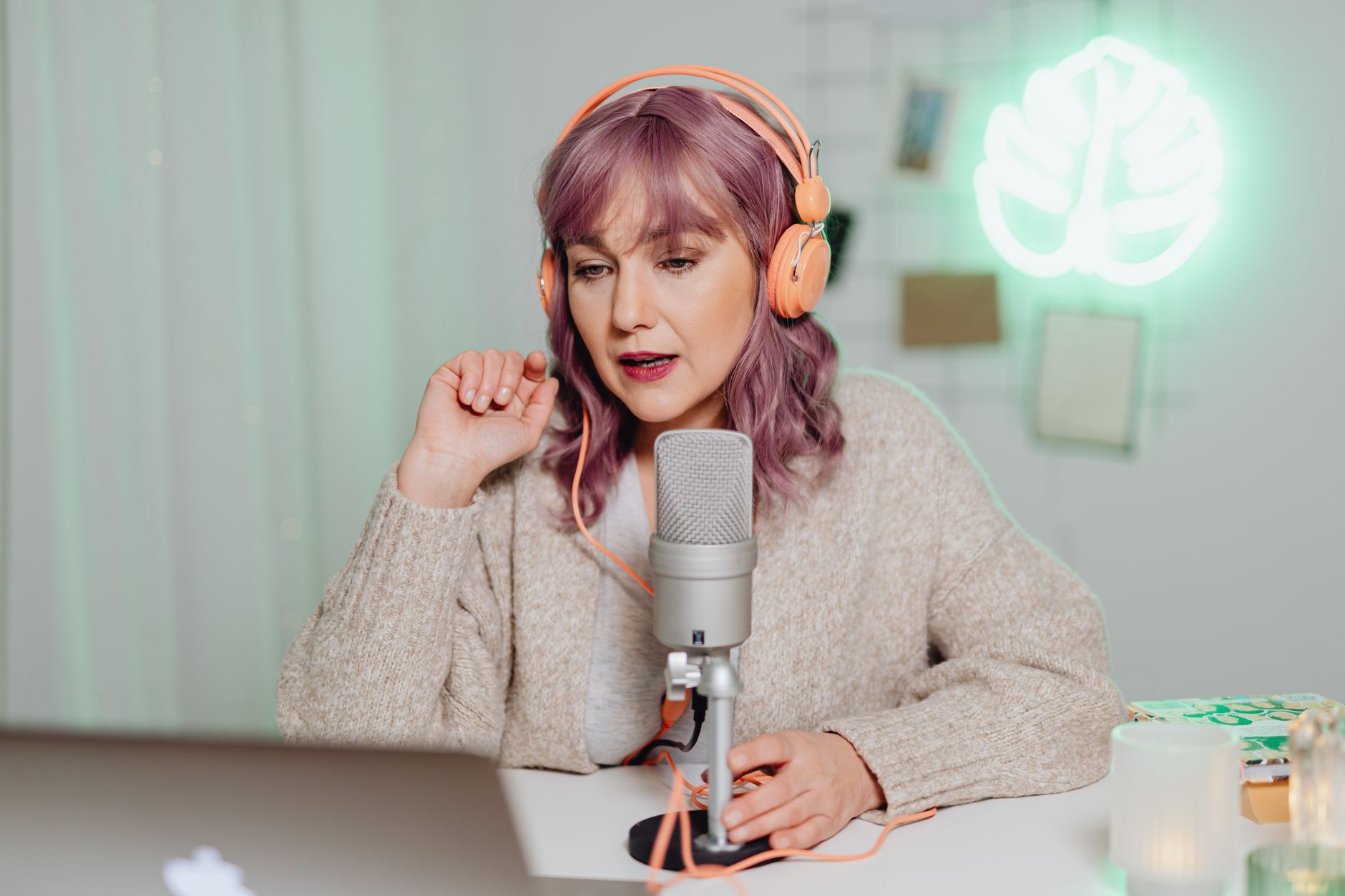 A woman with purple hair and orange headphones speaks into a podcast microphone