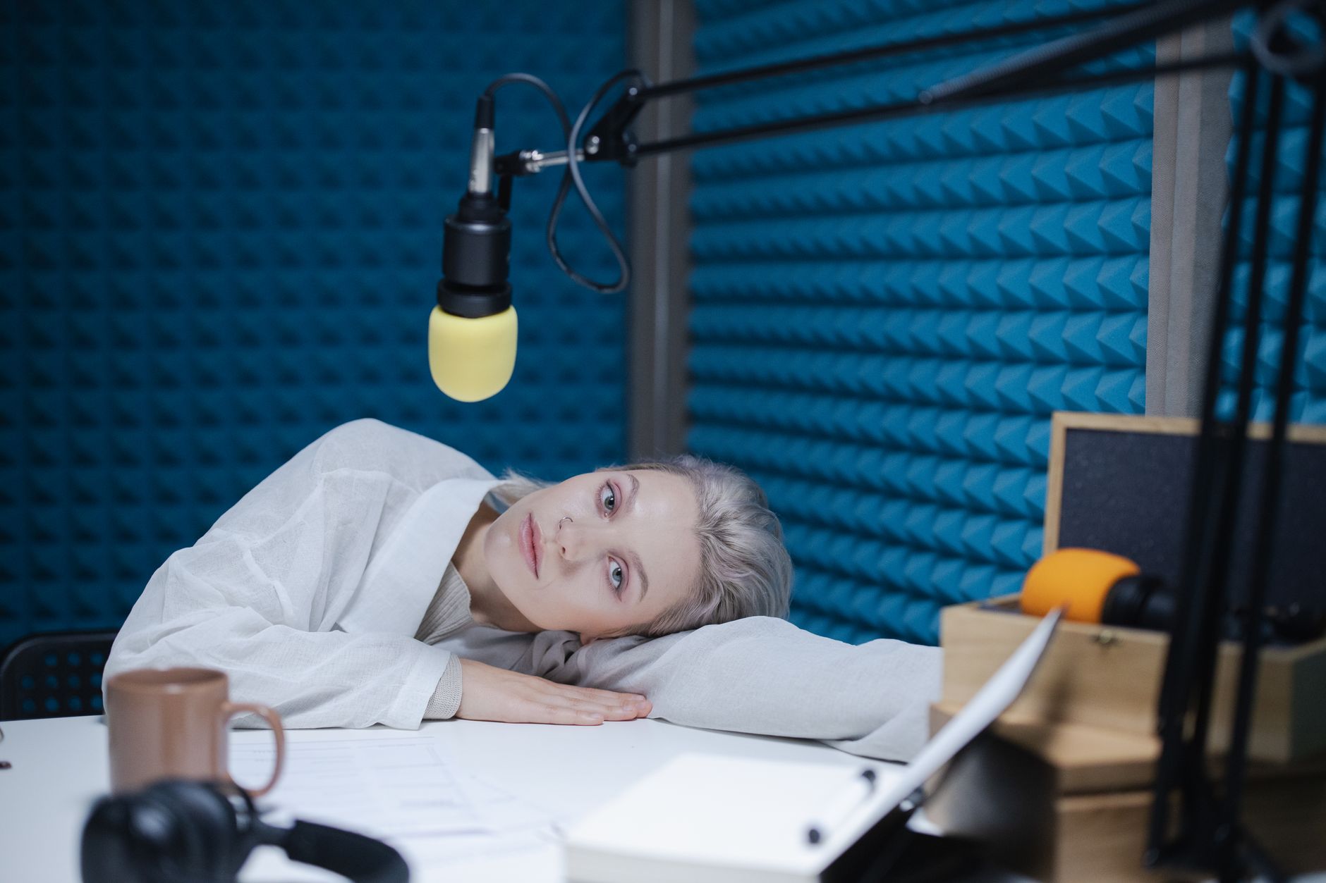A woman rests her head on a desk beneath a suspended microphone
