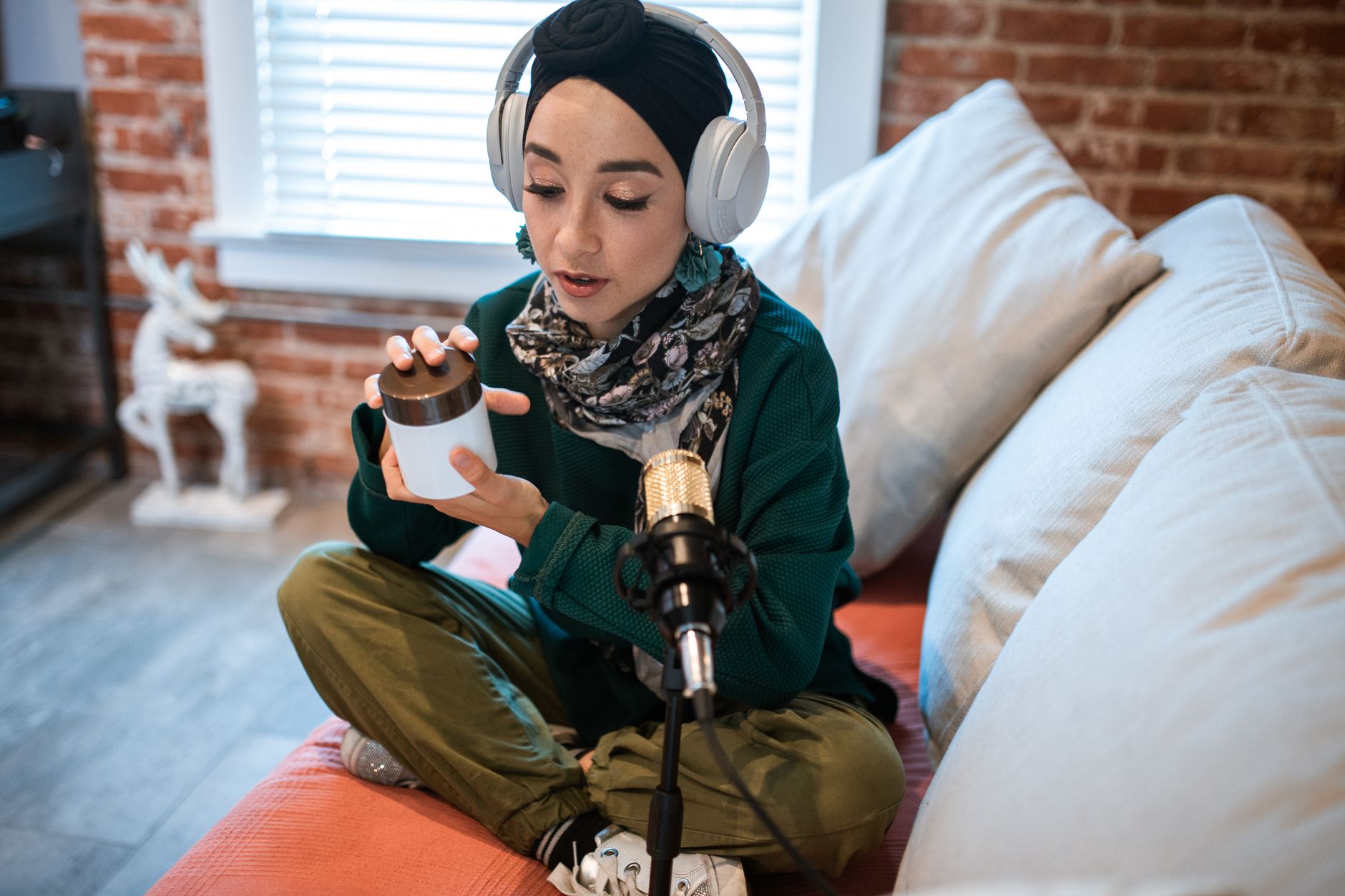 Woman in headphones recording a podcast, holding a product jar on a couch