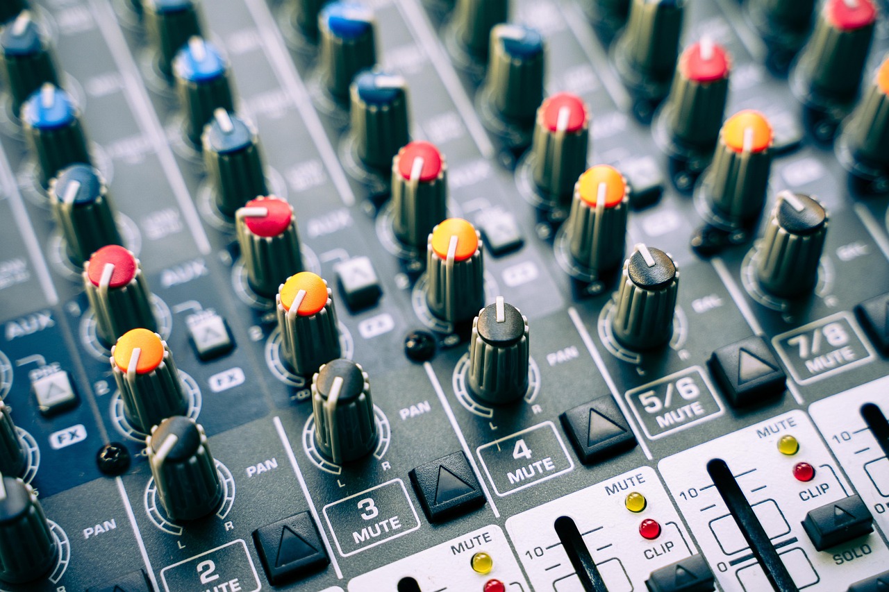 A close-up view of an audio mixer with many colorful knobs and faders