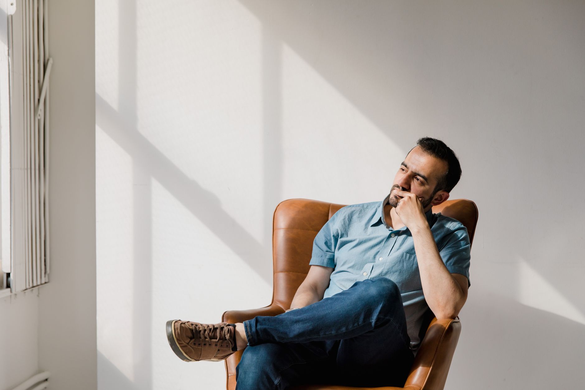 A thoughtful man sits in a chair, contemplating with shadows on the wall