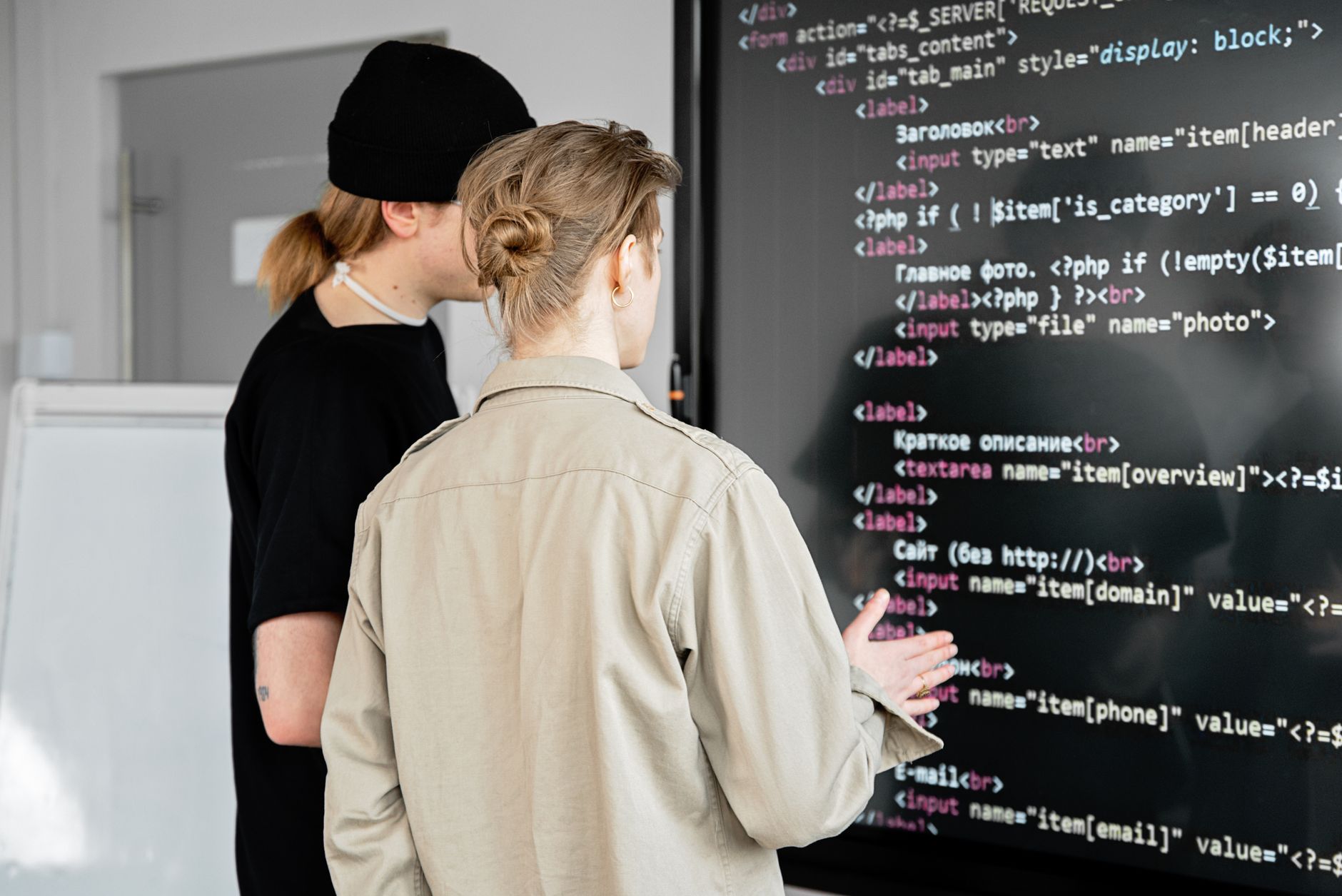 Two developers discussing code on a large screen, building a website