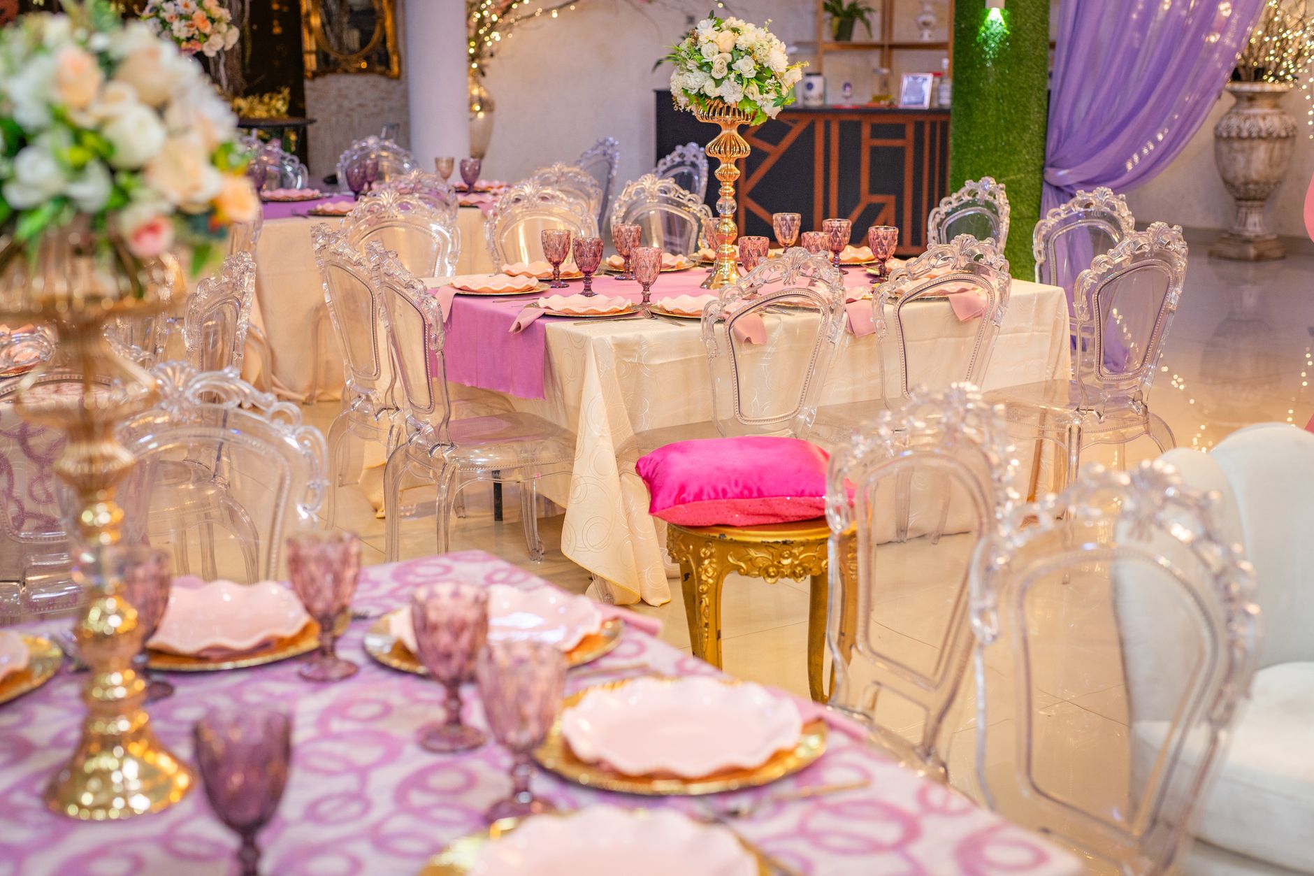 Elegant event tables with pink and purple decor and clear chairs in a venue