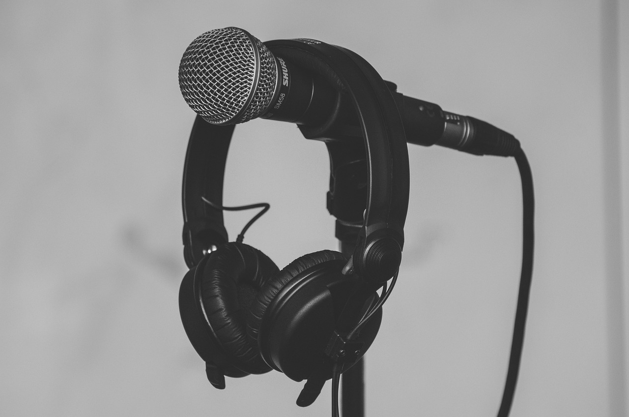 A black microphone and headphones hang from a stand, ready for recording podcasts