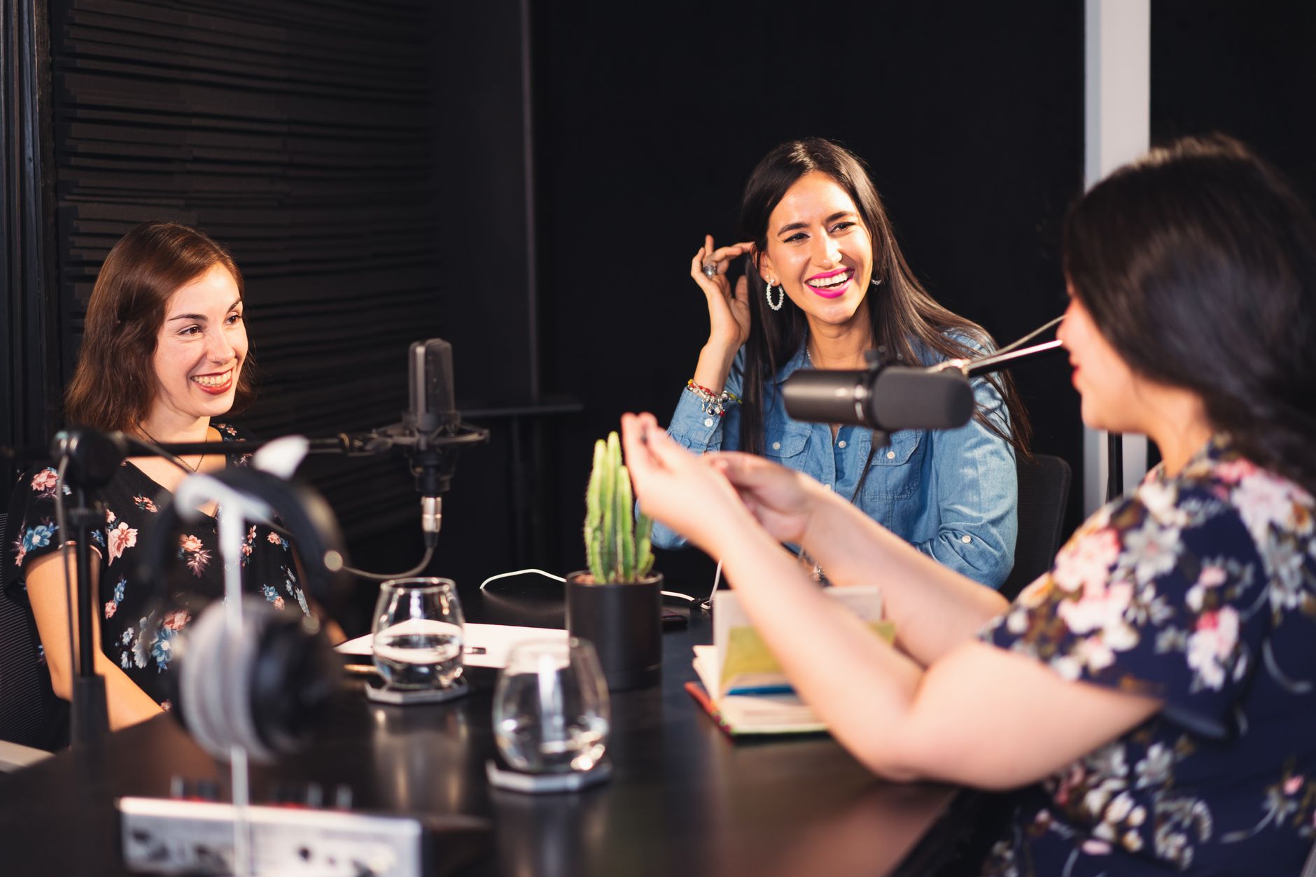 Three women smiling and talking during a podcast recording session with microphones