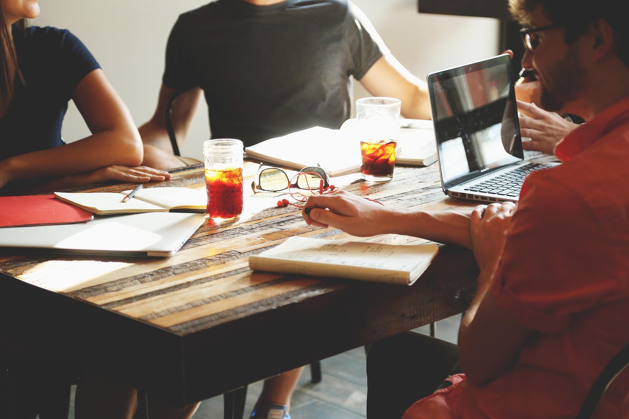 People collaborate at a wooden table with laptops, notebooks, and drinks for a digital agency