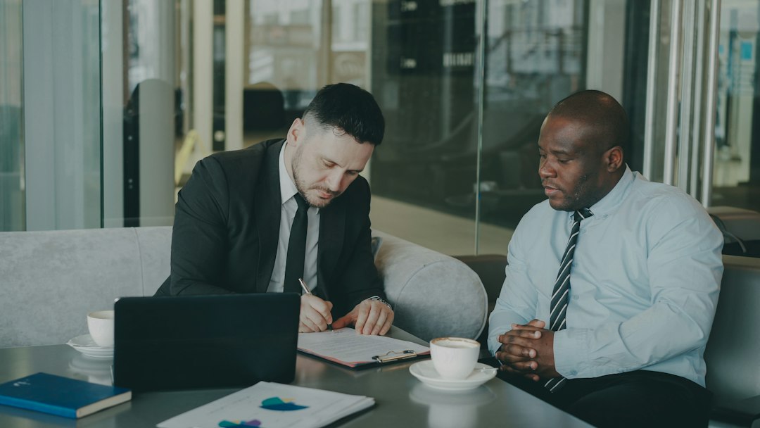 Two businessmen review and sign legal documents during a corporate compliance meeting
