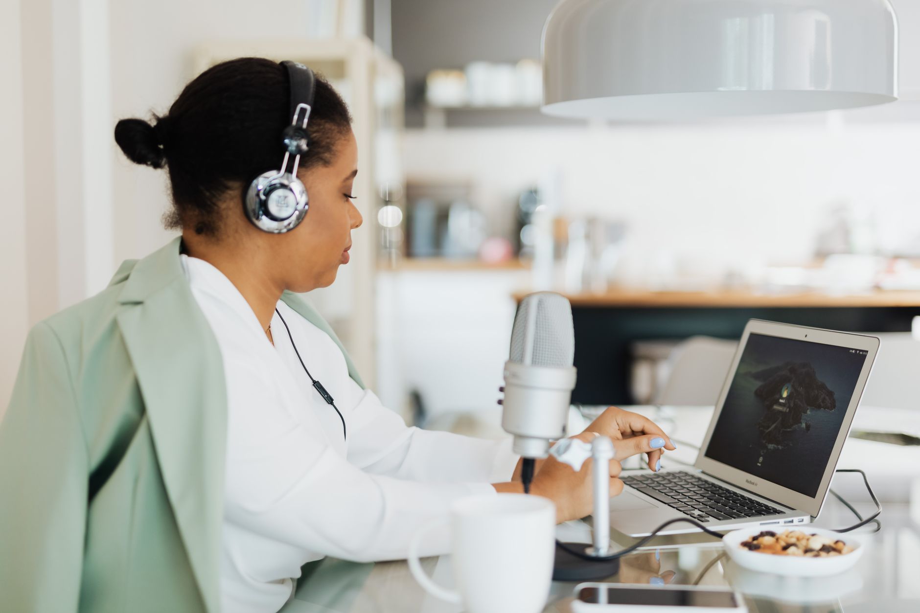 A woman wearing headphones sits at a desk with a laptop and microphone