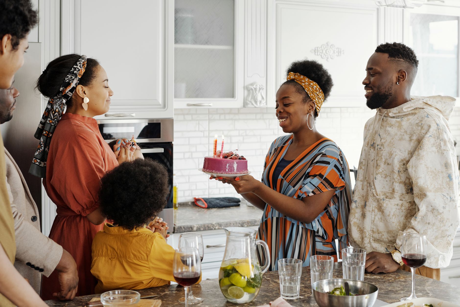 Family celebrates a milestone birthday in a kitchen with a cake and lit candles