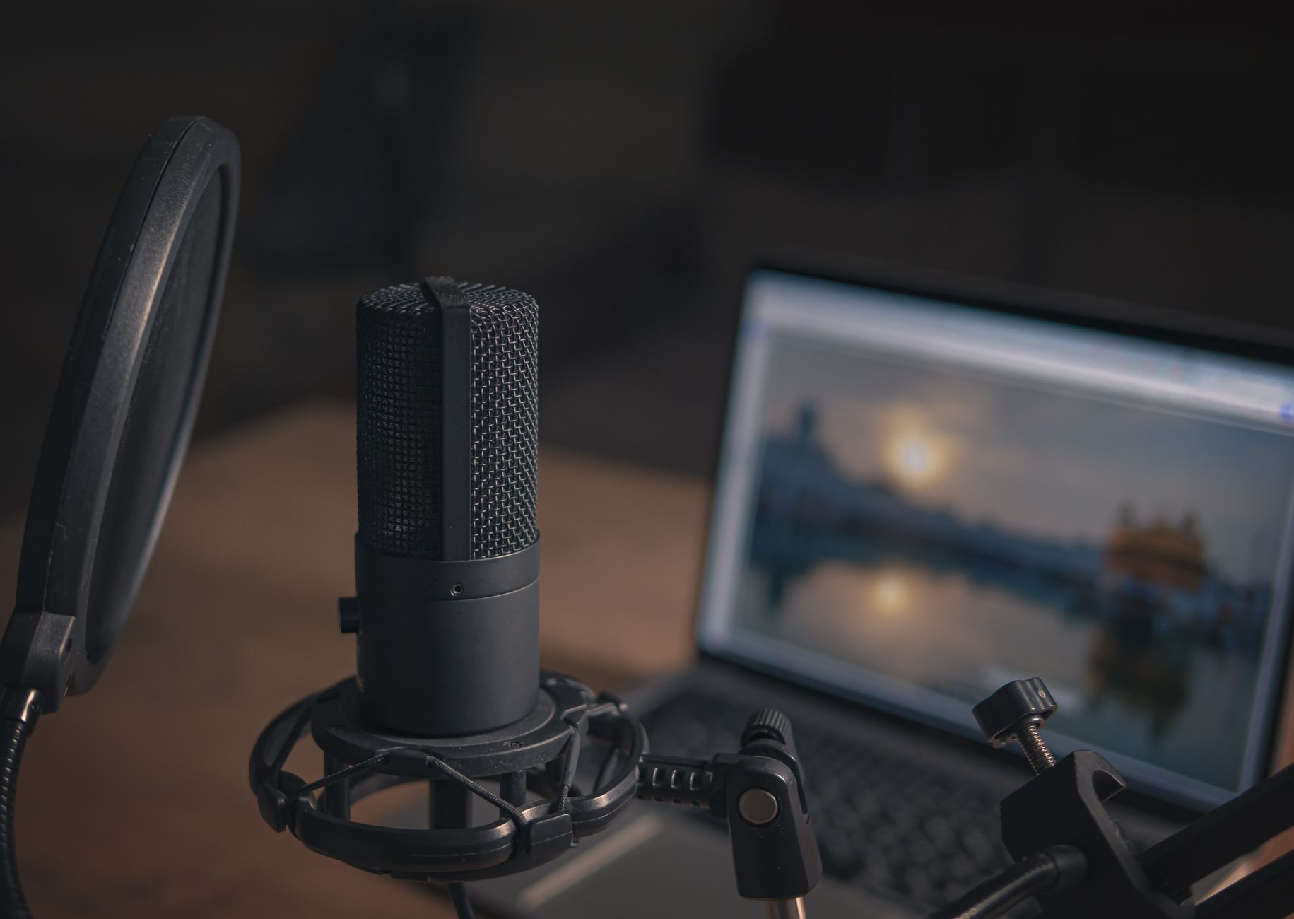 A podcast microphone and pop filter with a laptop in the blurred background