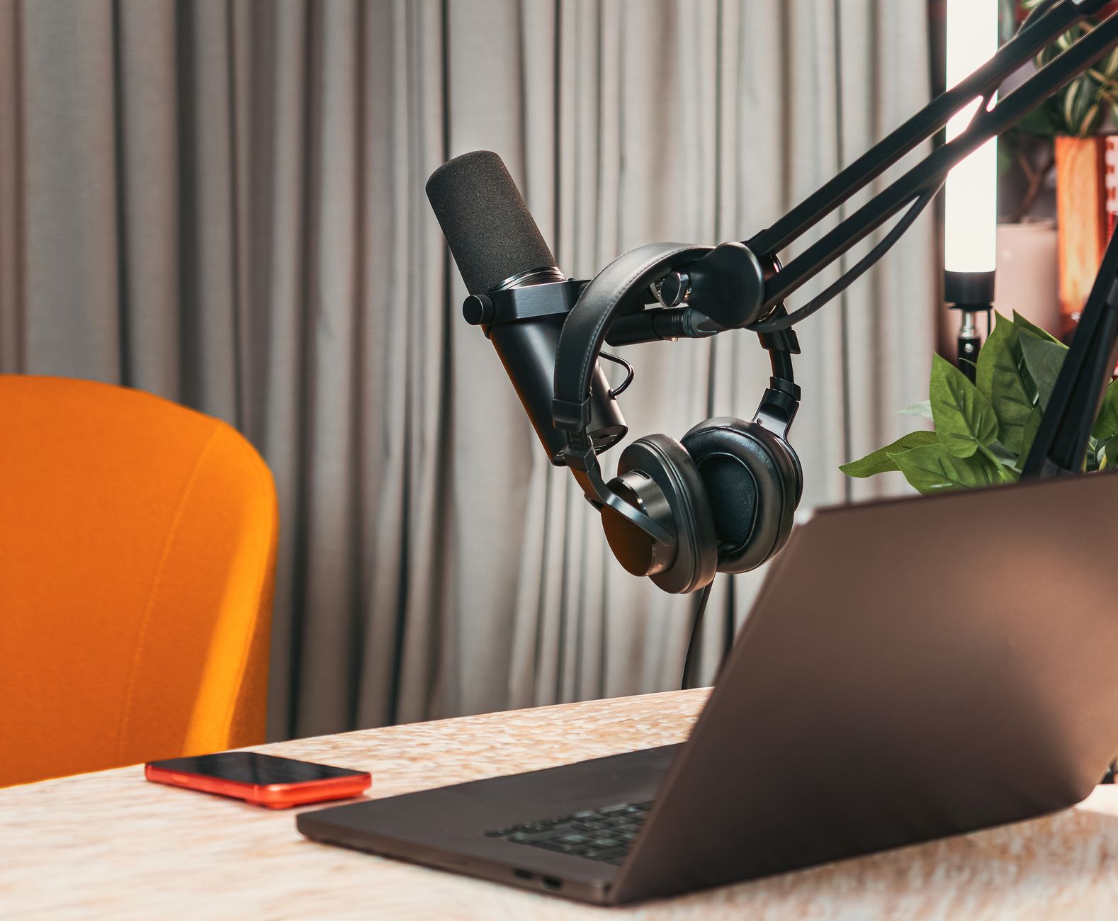 A microphone and headphones hang on a boom arm beside an open laptop