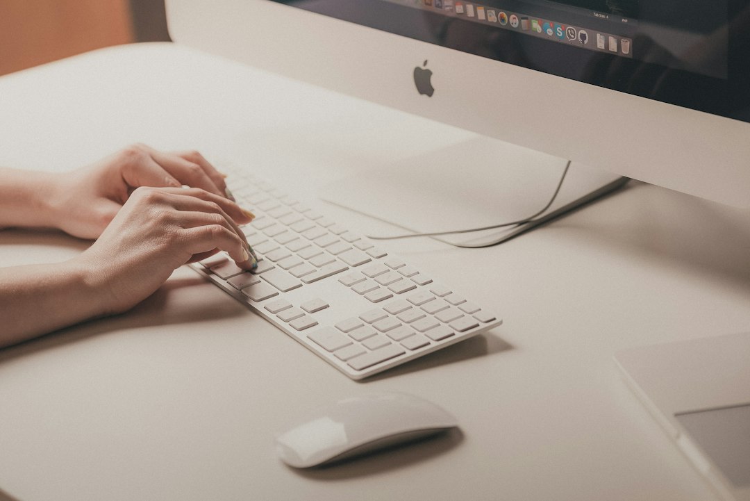 A person types on a white keyboard in front of a computer monitor