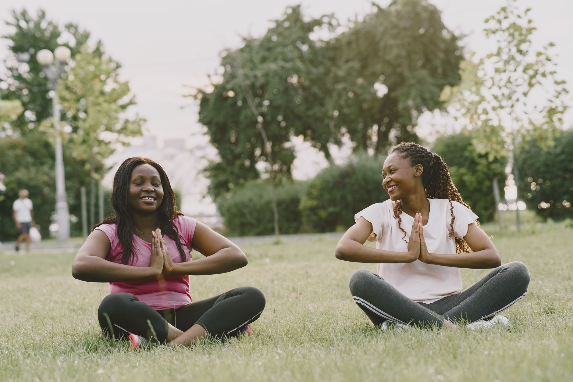 Two women meditating in prayer pose on grass, enjoying outdoor wellness