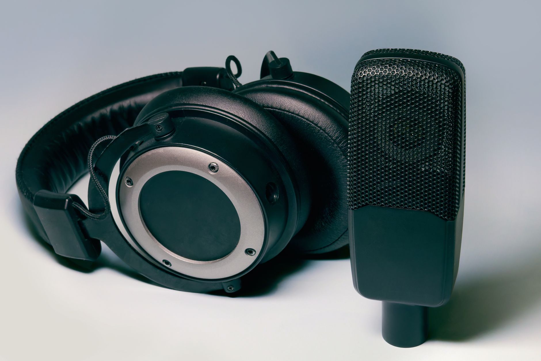 Black over-ear headphones rest next to a condenser microphone for podcast recording