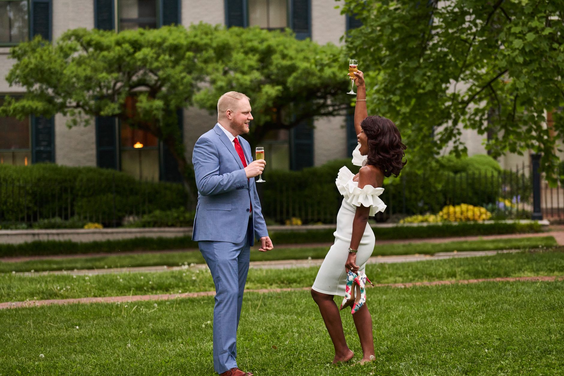 Engaged couple toasting with champagne glasses on a lush green lawn