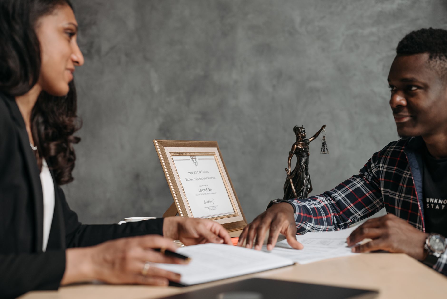 A lawyer and client discuss legal documents with a Lady Justice statue nearby