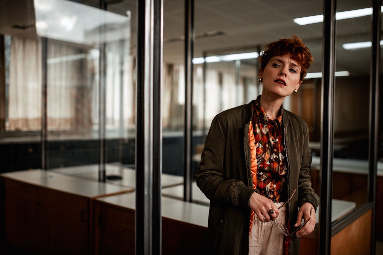 Woman with short hair in a bomber jacket holding glasses in an office