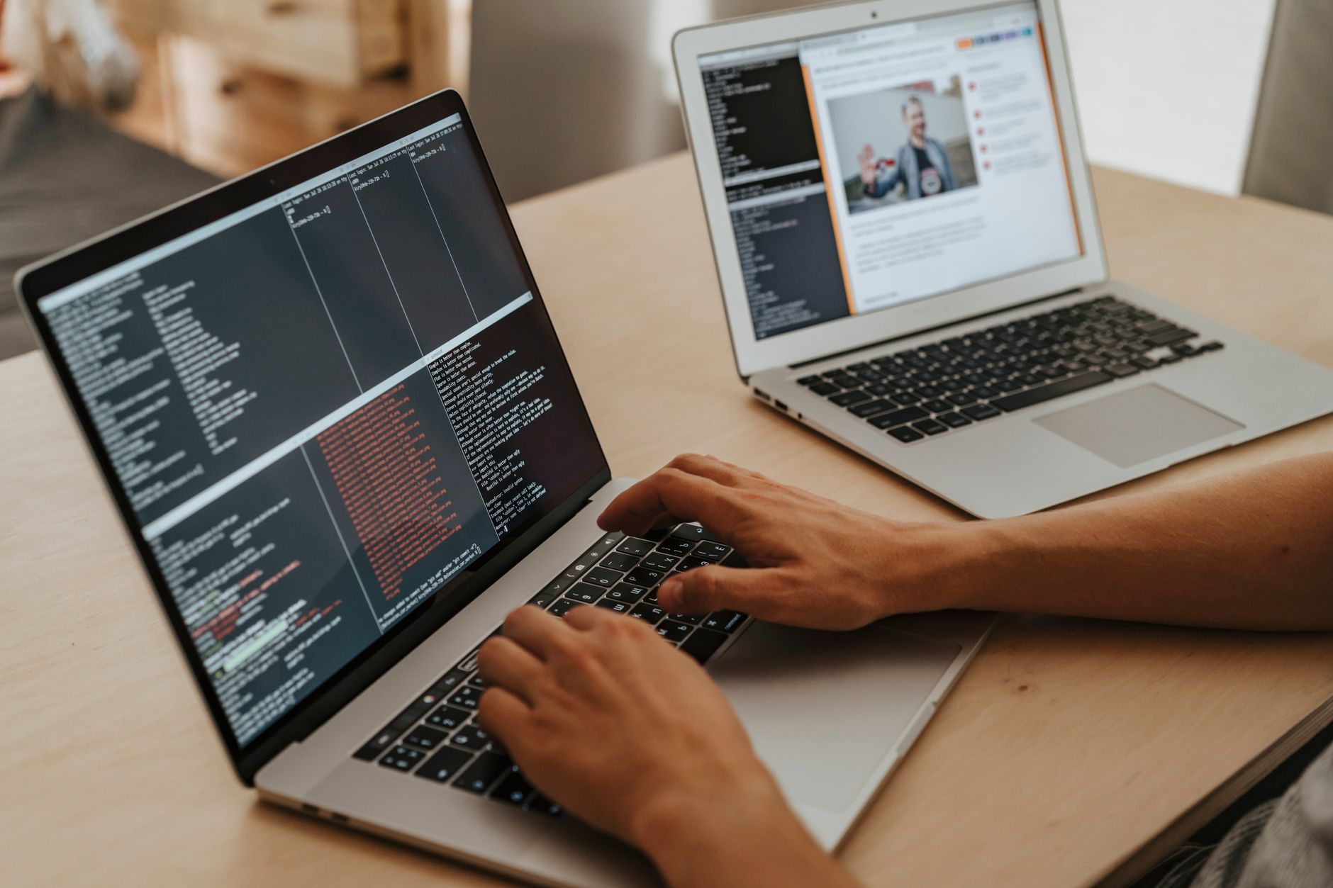 Hands typing on a laptop displaying code, with another laptop showing a website