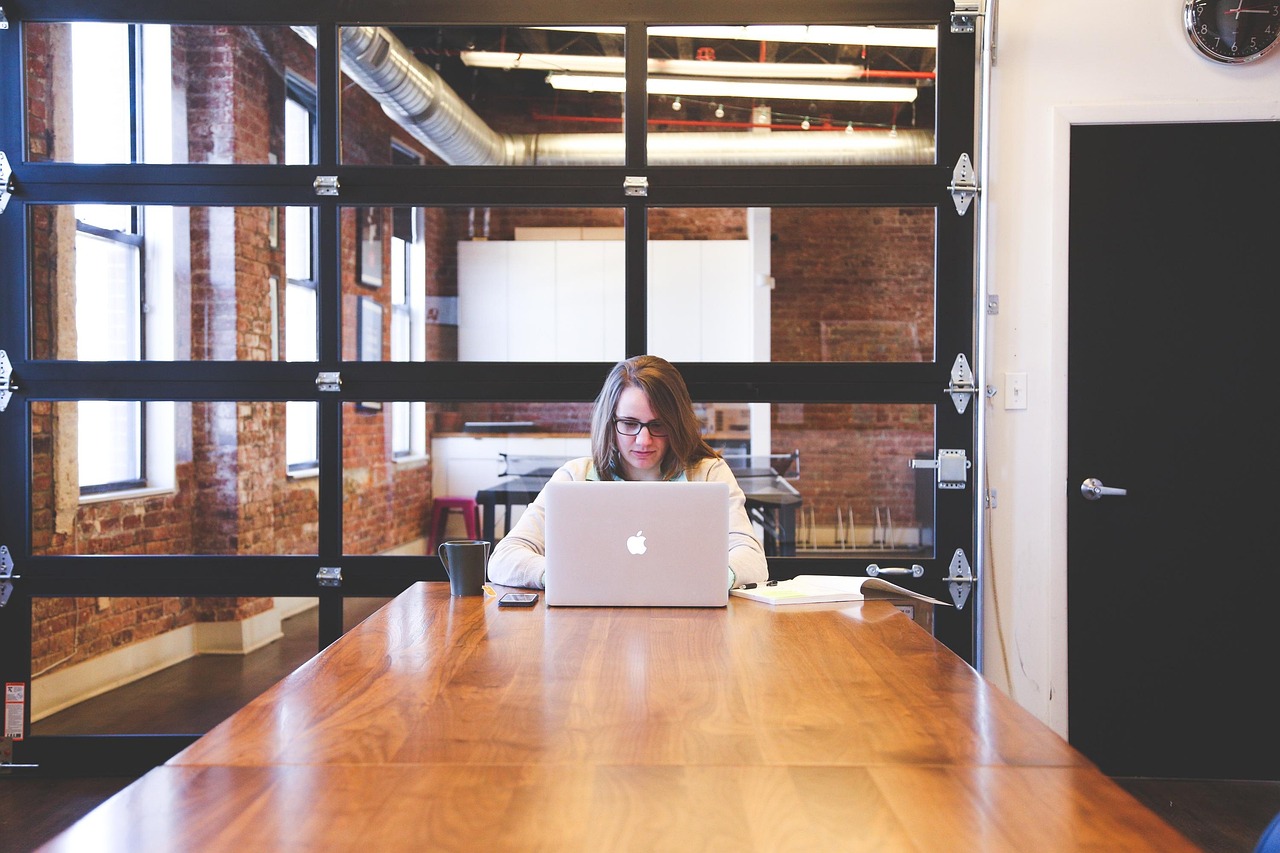 Woman working on a laptop at a large wooden table in a modern office