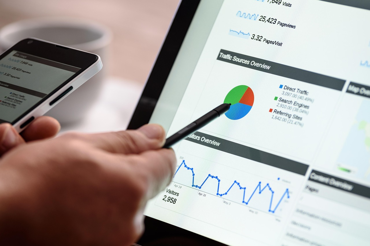 Hand points stylus at tablet showing website analytics data and graphs