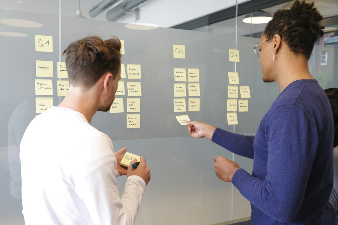 Two marketing professionals collaborate on project tasks written on sticky notes on a glass wall