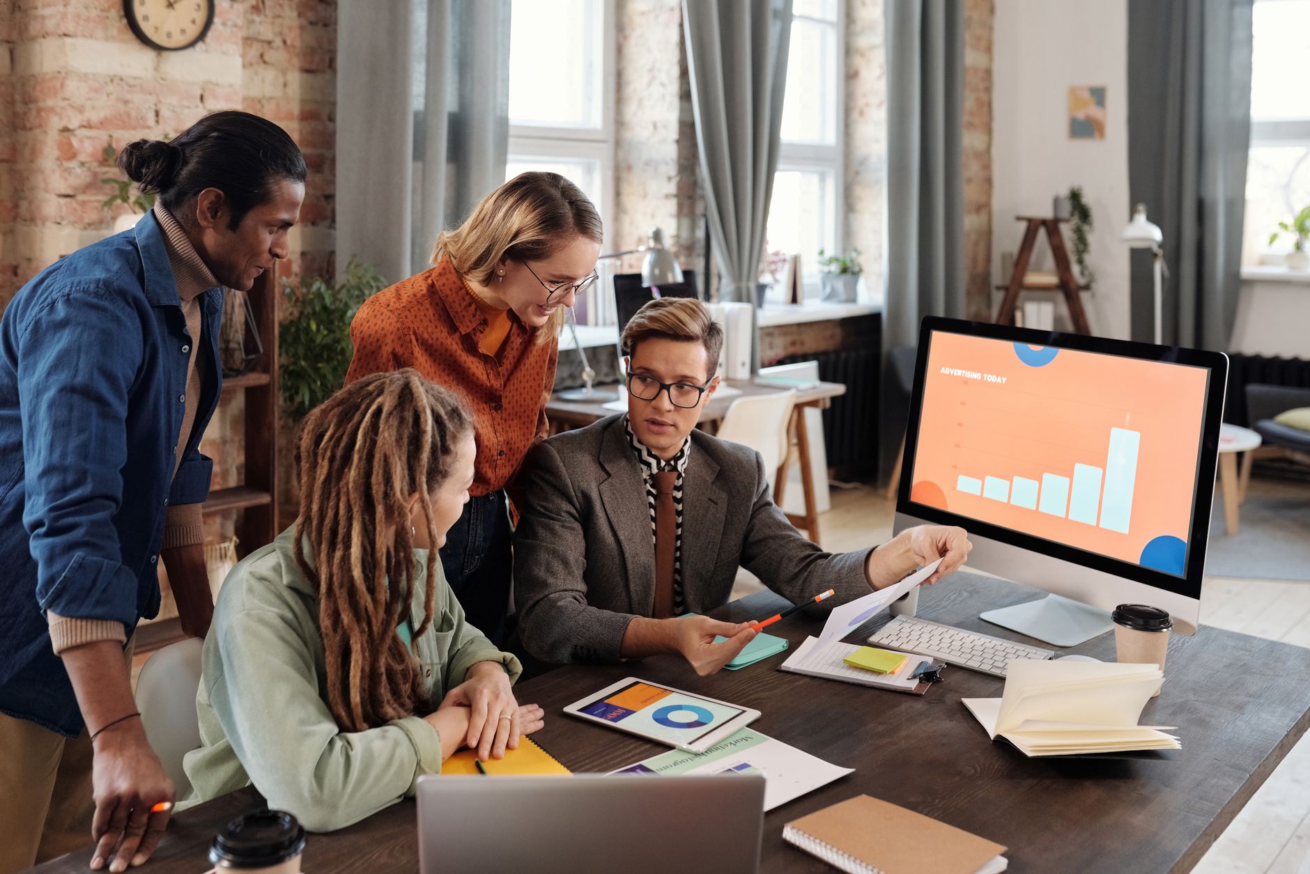 Four diverse professionals analyze digital advertising data on screens and documents
