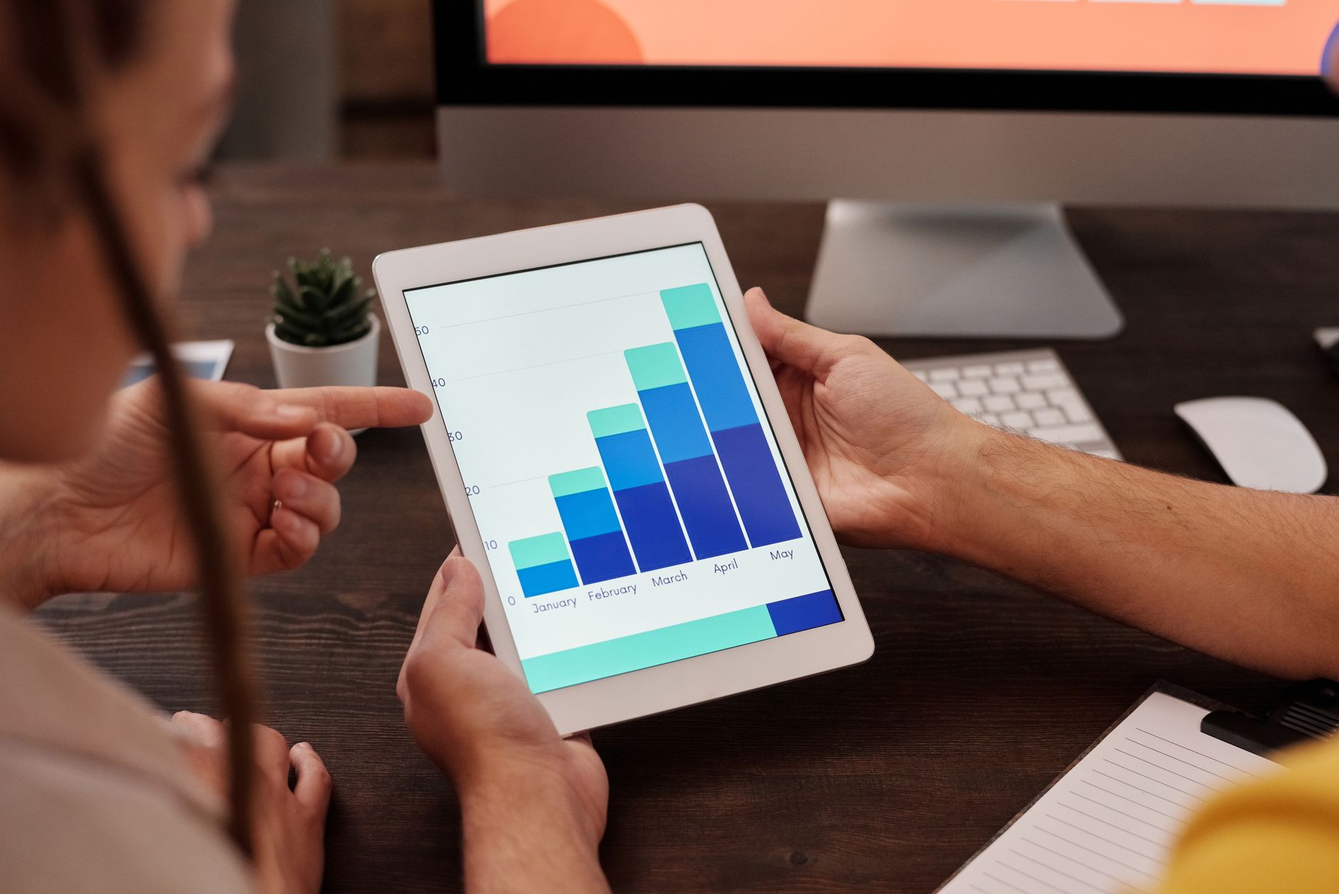Two people analyze a growing bar graph on a tablet, showing monthly progress