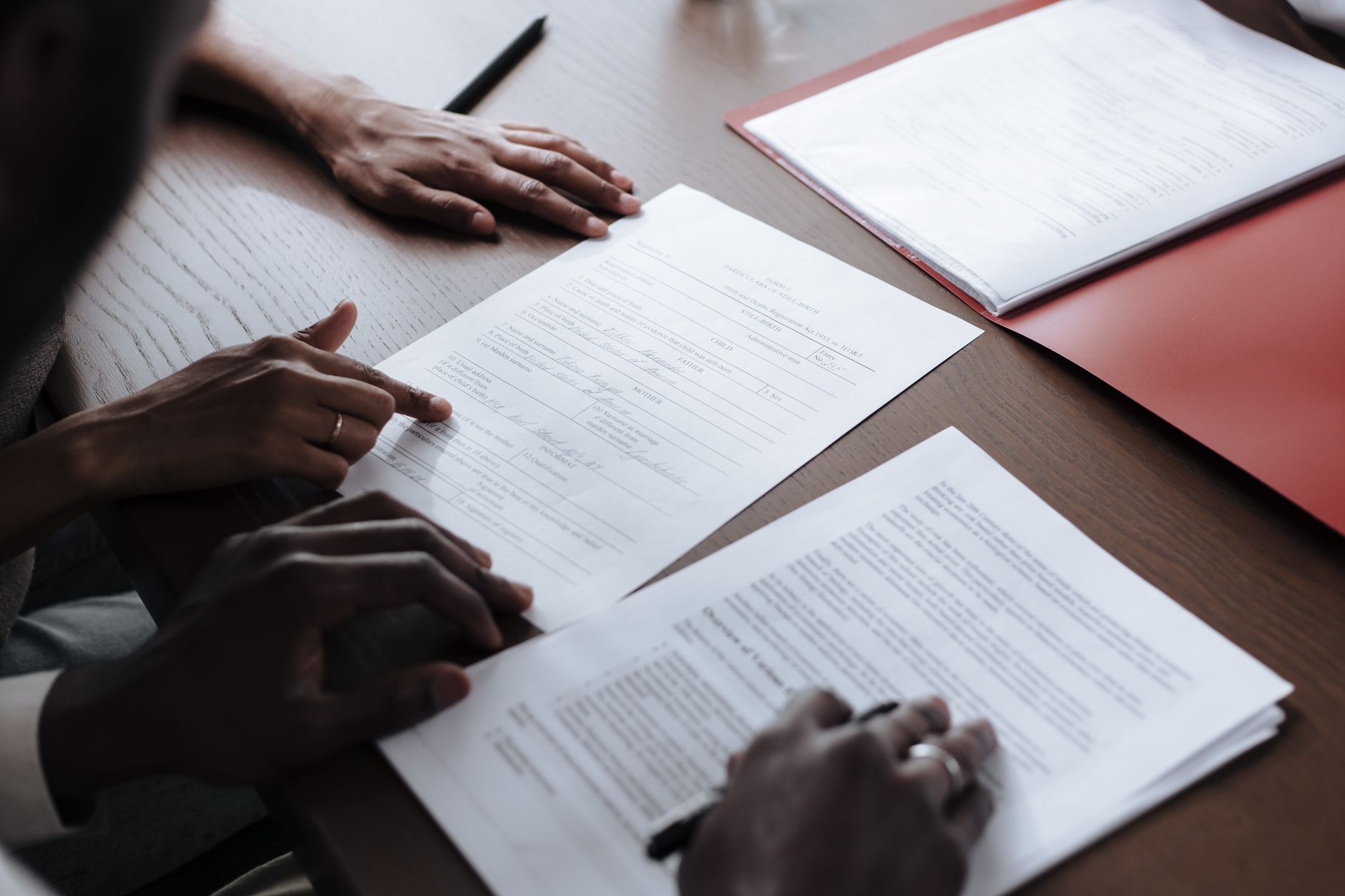 Two people reviewing paperwork and a formal document on a wooden table