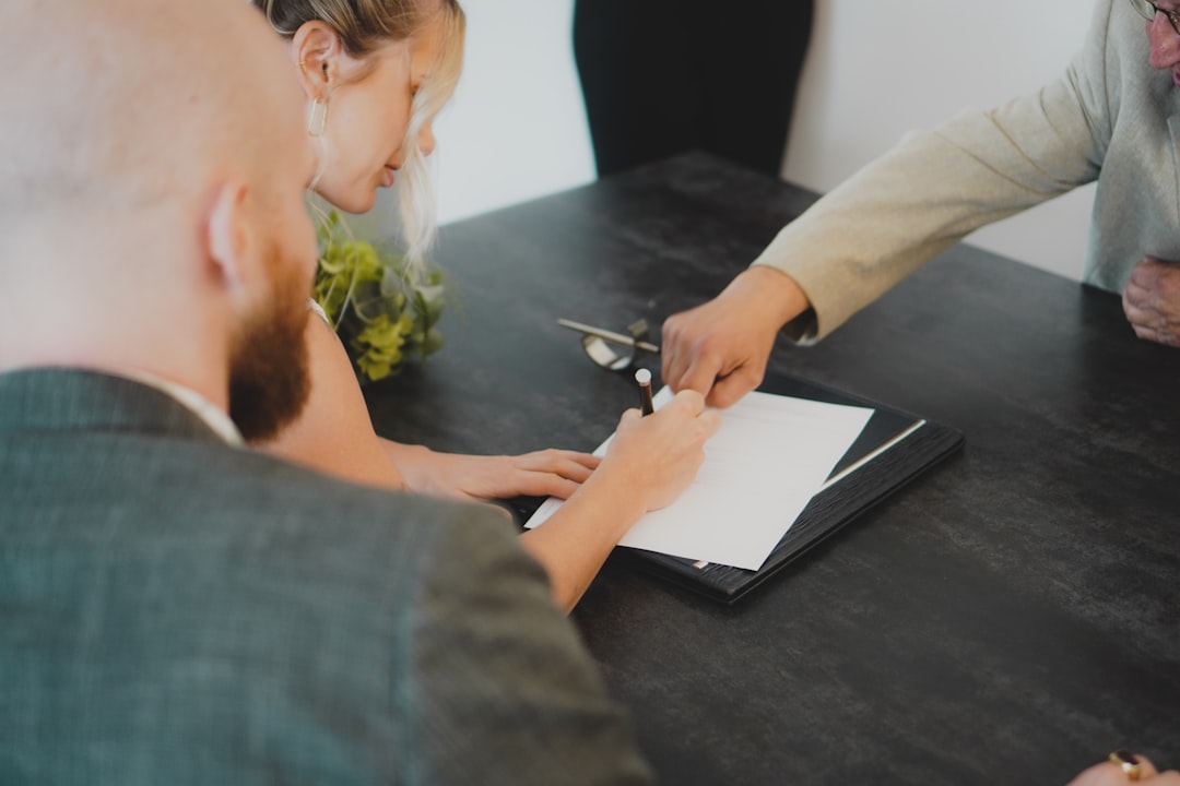 A woman signs a legal document with guidance from another person