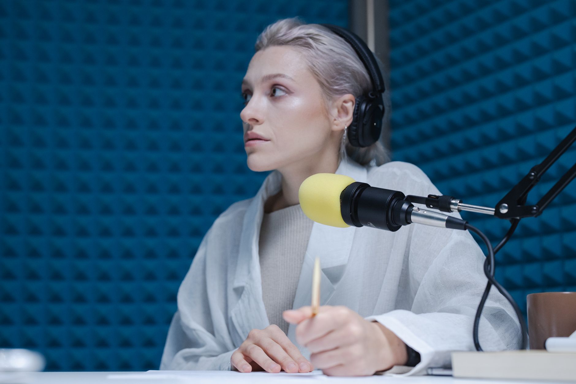 Young woman with headphones recording a podcast, holding a pencil and looking thoughtful