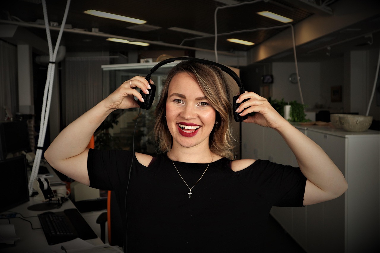 A smiling woman holding headphones ready to record or listen to a podcast