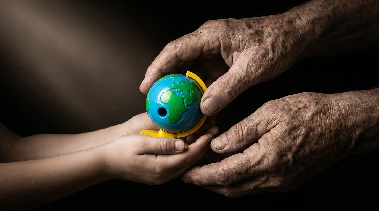 A child's hands receiving a small globe from an older person's hands