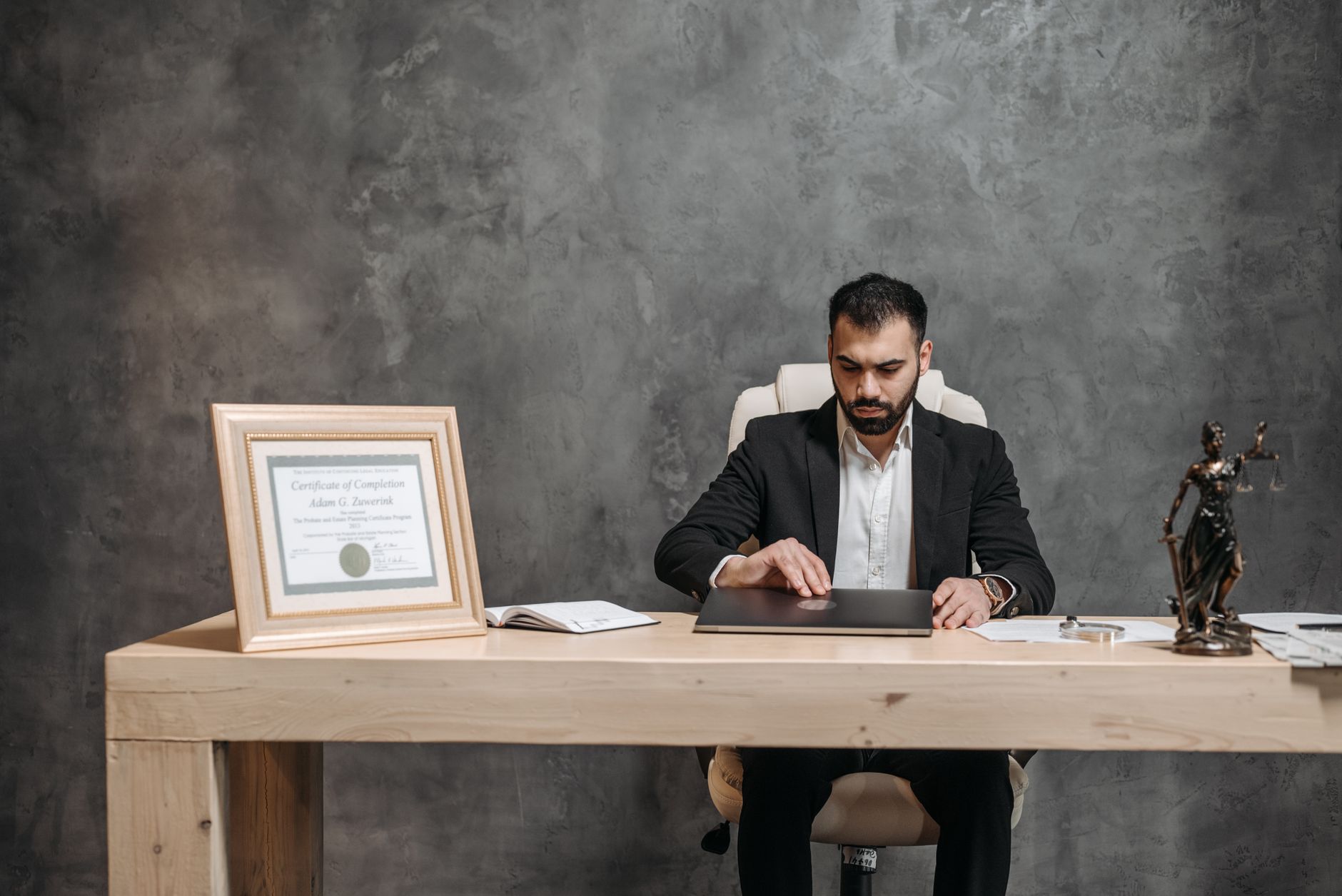 Man in suit closing a laptop on a desk with a Lady Justice statue