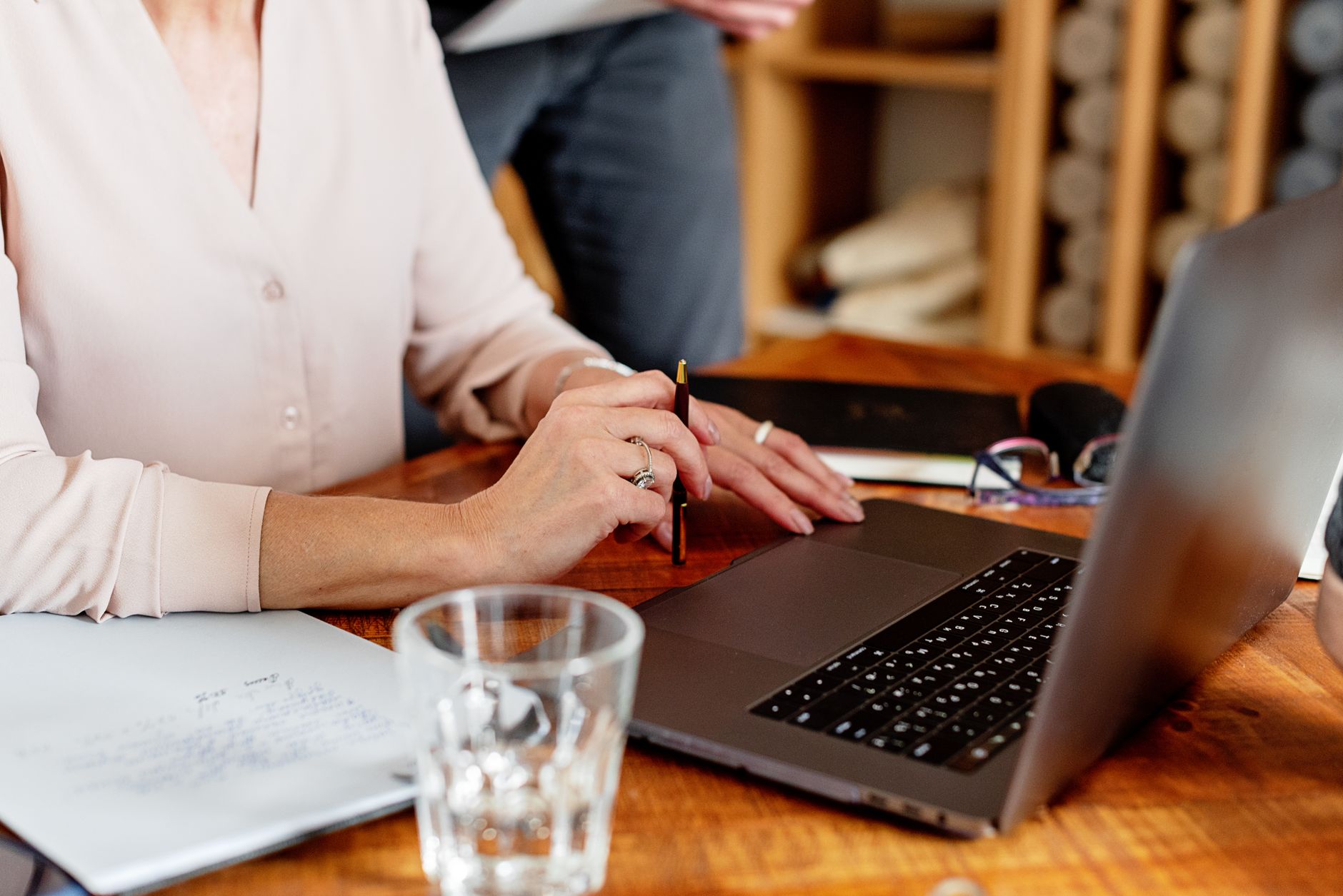Woman's hands holding a pen, working on a laptop at a wooden table