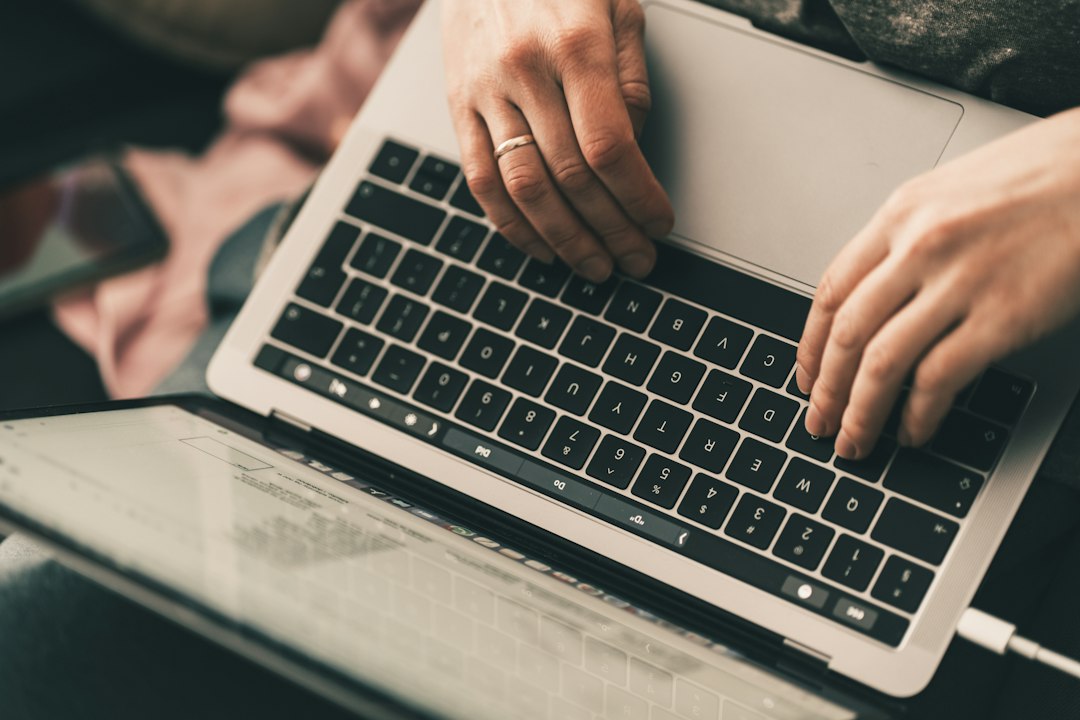 Two hands type on the black keyboard of an open silver laptop