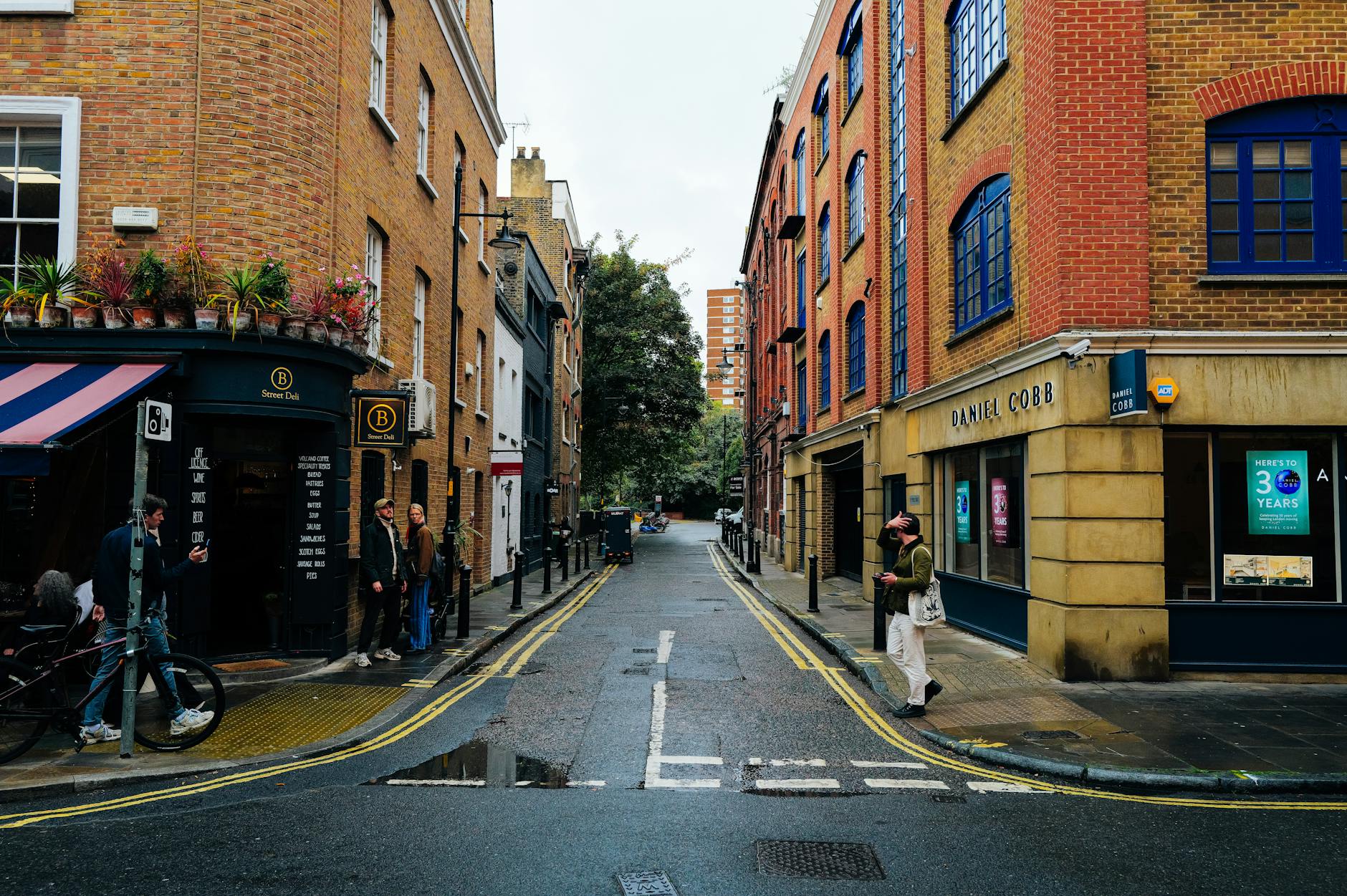 A narrow street with brick buildings and small shops, people walking casually