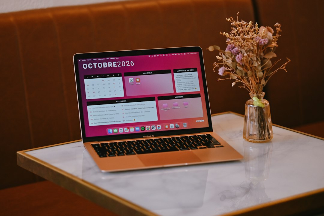 An open laptop showing a calendar sits beside a vase of dried flowers