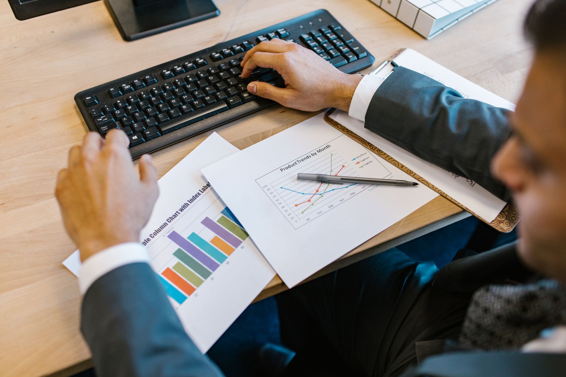 A person in a suit types on a keyboard beside printed charts