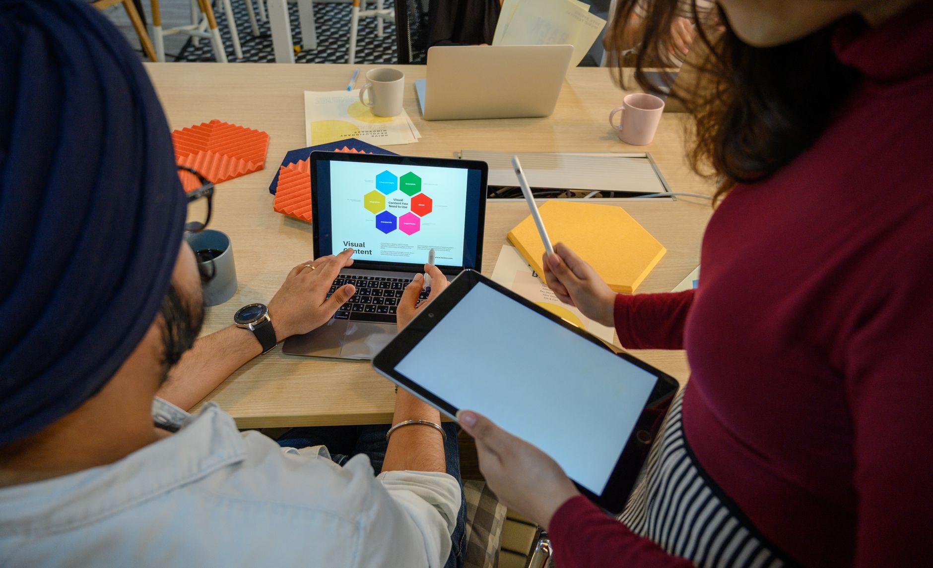 Two people collaborate on a laptop showing a "Visual Content" diagram and a tablet
