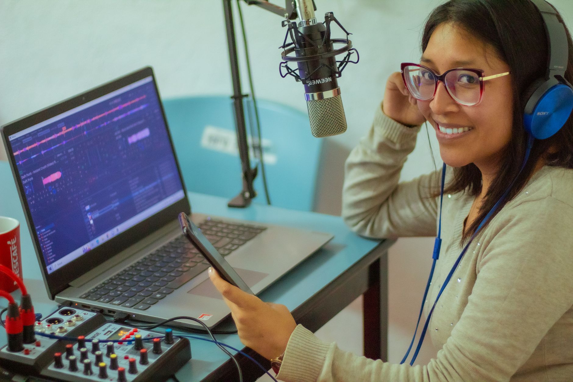 Smiling woman wearing headphones, recording a podcast with professional equipment and laptop