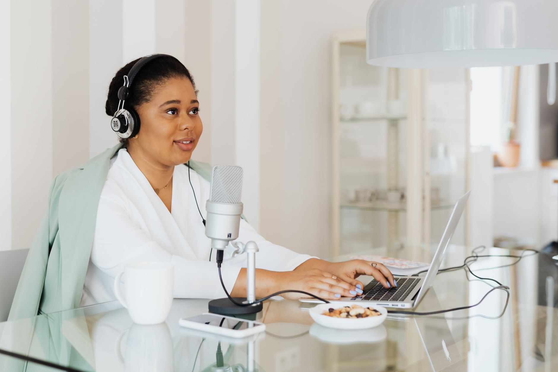 Woman with headphones and microphone records podcast while typing on a laptop