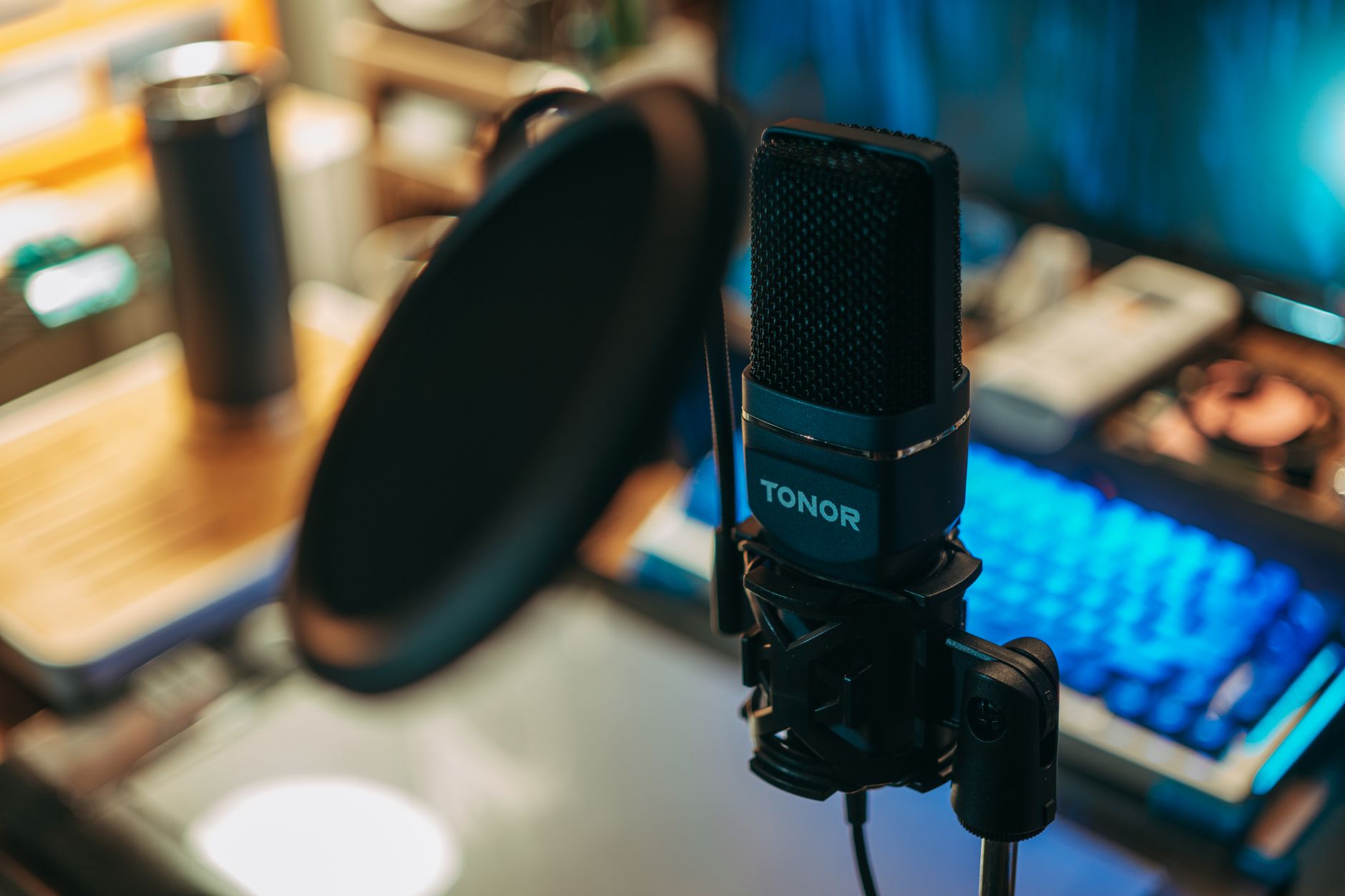 A black podcast microphone with a pop filter and glowing keyboard in the background